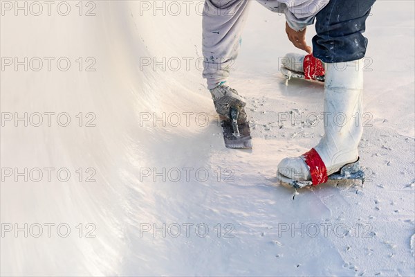 Worker wearing spiked shoes smoothing wet pool plaster with trowel