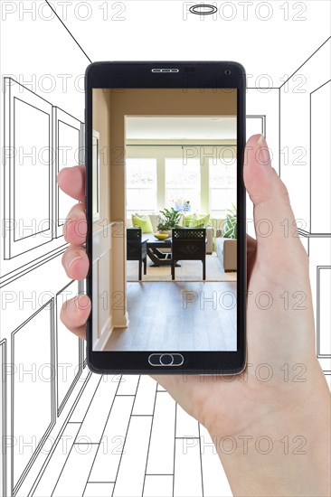 Hand holding smart phone displaying photo of the house hallway drawing behind