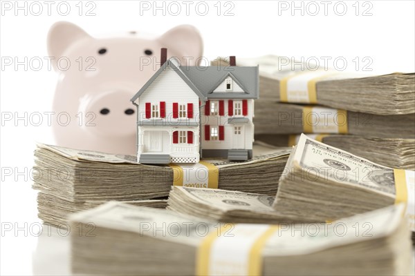 Small house and piggy bank with stacks of hundred dollar bills isolated on a white background