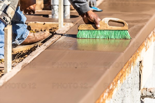 Construction worker using brush on wet cement forming coping around new pool