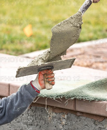 Construction worker placing wet cement on platter for tile worker at pool construction site