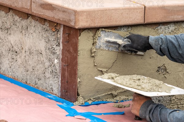 Tile worker applying cement with trowel at pool construction site