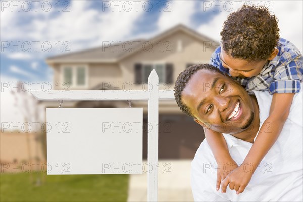 Happy african american father and mixed-race son in front of blank real estate sign and new house