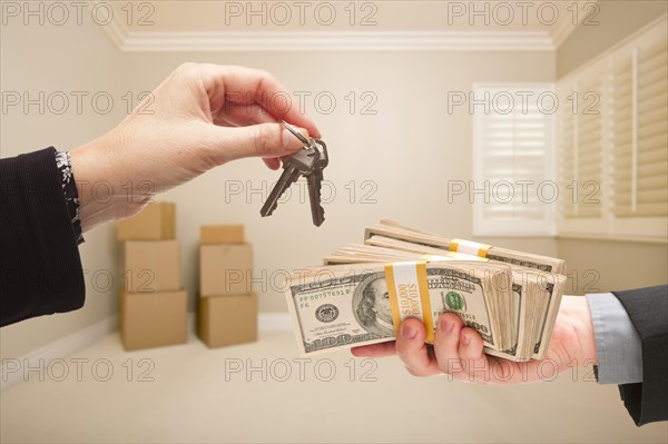 Man and woman handing over cash for house keys inside empty tan room with boxes