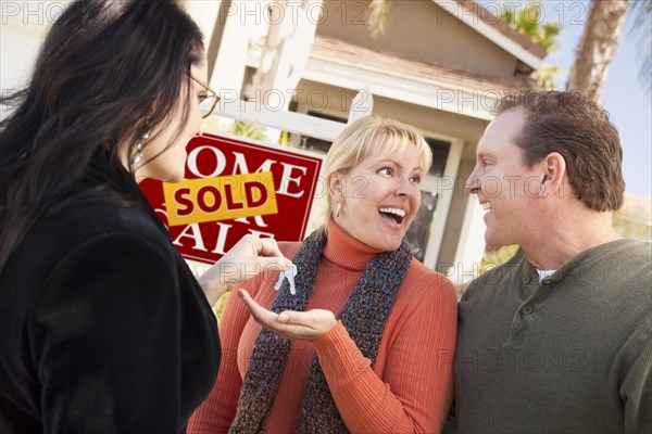 Hispanic female real estate agent handing over new house keys to excited couple