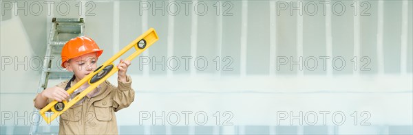 Cute young boy dressed as contractor holding level against dywall banner background with ladder