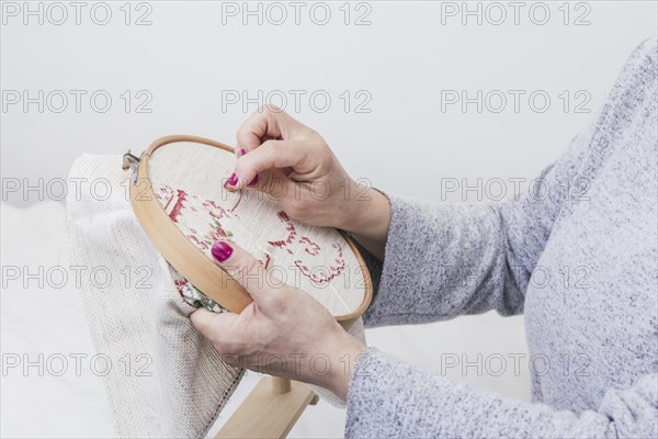 woman s hand cross stitching pattern on a hoop against white background