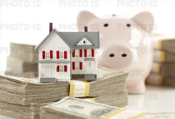 Small house and piggy bank with stacks of hundred dollar bills isolated on a white background