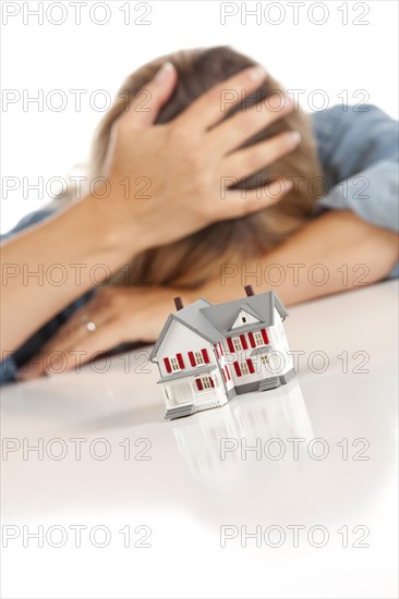 Woman with head in hand behind model home on a white surface