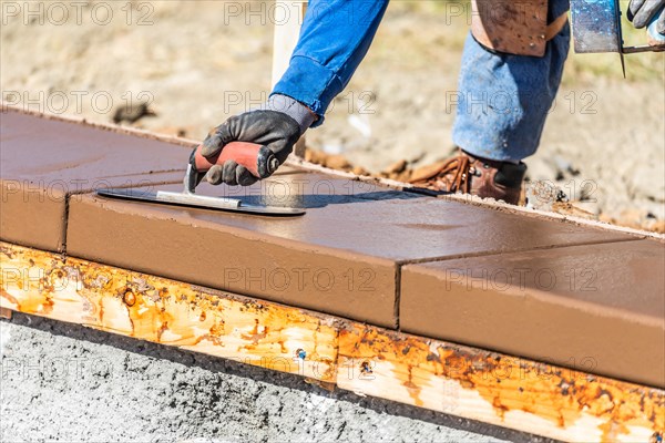 Construction worker using trowel on wet cement forming coping around new pool