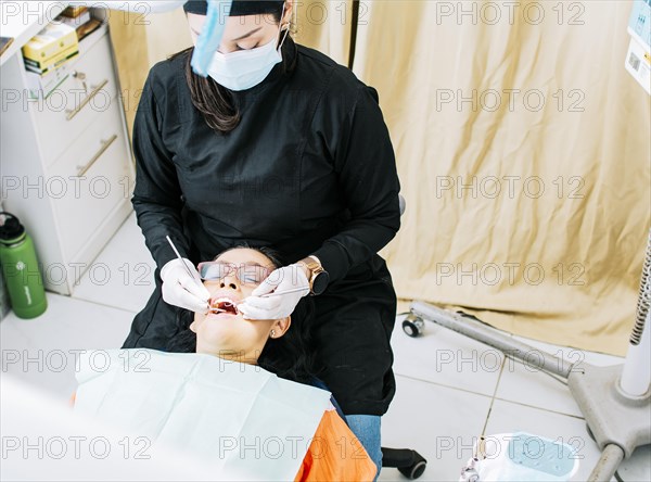 Woman dentist doing endodontics to woman patient.  Dentist with patient lying down. Dentist examining mouth to patient. Dentist performing stomatology