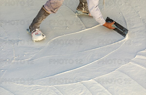 Worker wearing spiked shoes smoothing wet pool plaster with trowel
