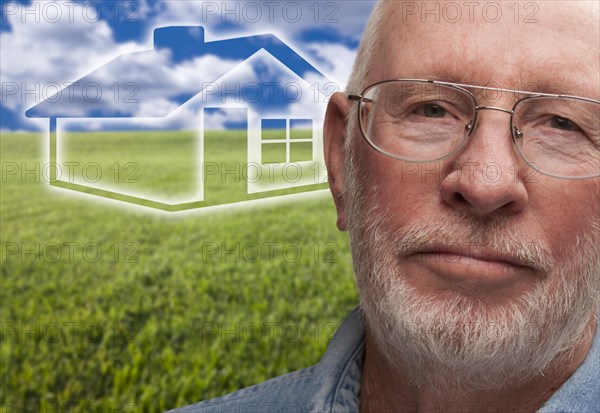 Melancholy senior man with green grass field and ghosted house behind him