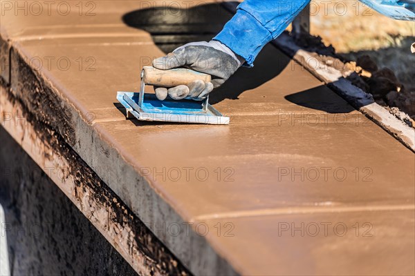 Construction worker using hand groover on wet cement forming coping around new pool