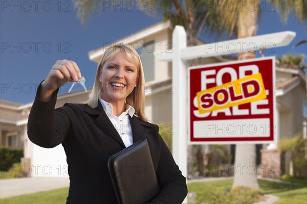 Female real estate agent handing over the house keys in front of a beautiful new home and real estate sign