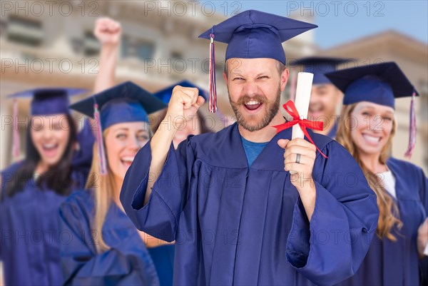 Proud male graduate in cap and gown in front of other graduates