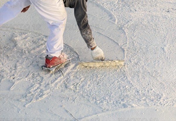 Worker wearing spiked shoes smoothing wet pool plaster with trowel
