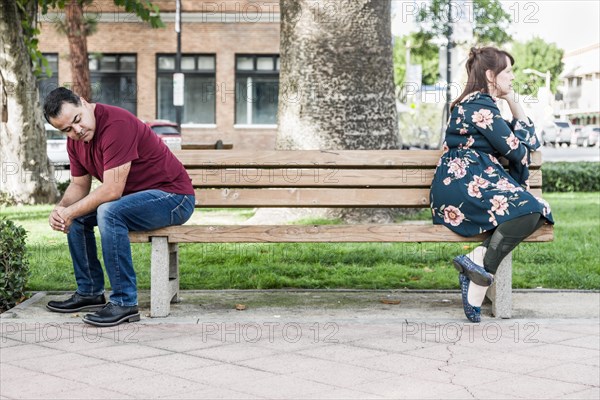 Unhappy mixed-race couple sitting facing away from each other on park bench