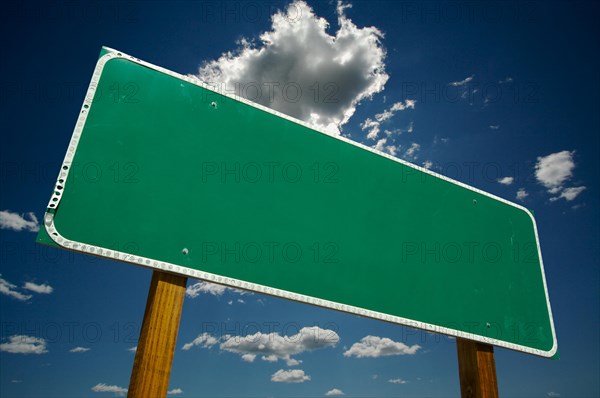 Blank green road sign on dramatic blue sky with clouds