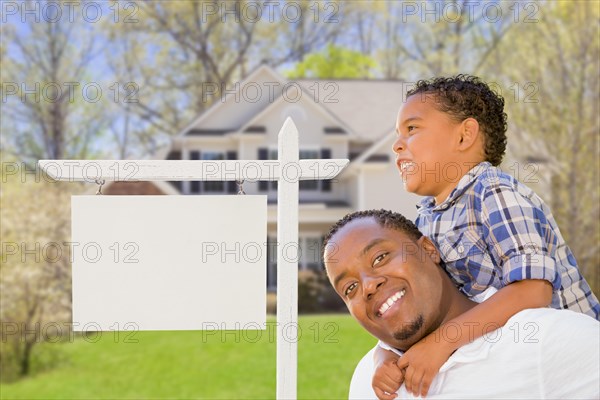 Happy african american father and mixed-race son in front of blank real estate sign and new house