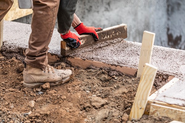 Construction worker leveling wet cement into wood framing