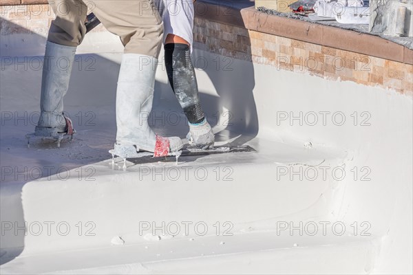 Worker wearing spiked shoes smoothing wet pool plaster with trowel