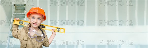 Cute young boy dressed as contractor holding level against dywall banner background with ladder