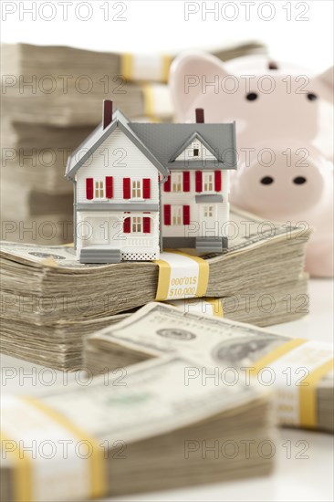 Small house and piggy bank with stacks of hundred dollar bills isolated on a white background