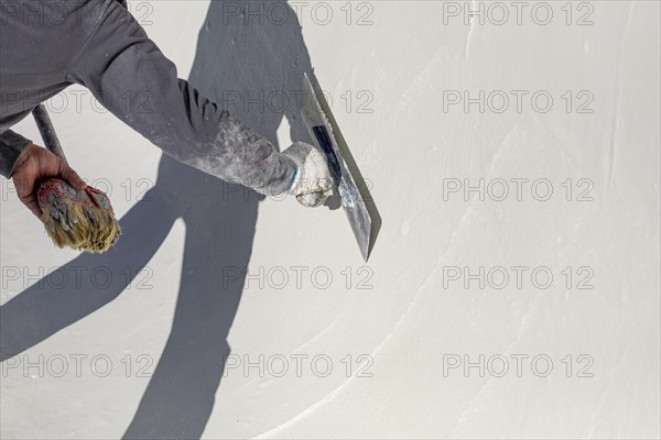 Worker smoothing wet pool plaster with trowel