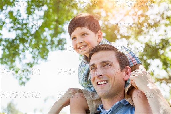 mixed-race father and son playing piggyback together in the park