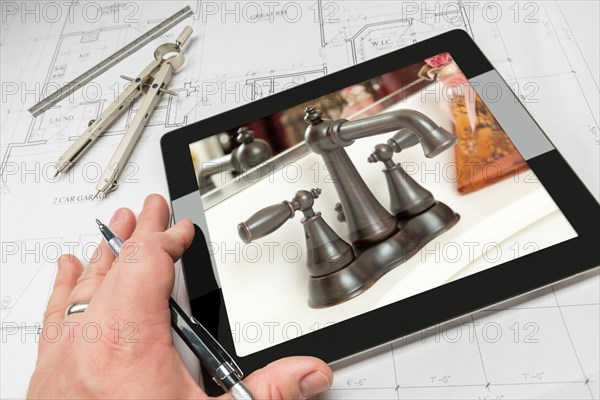 Hand of architect on computer tablet showing luxury bathroom details over house plans