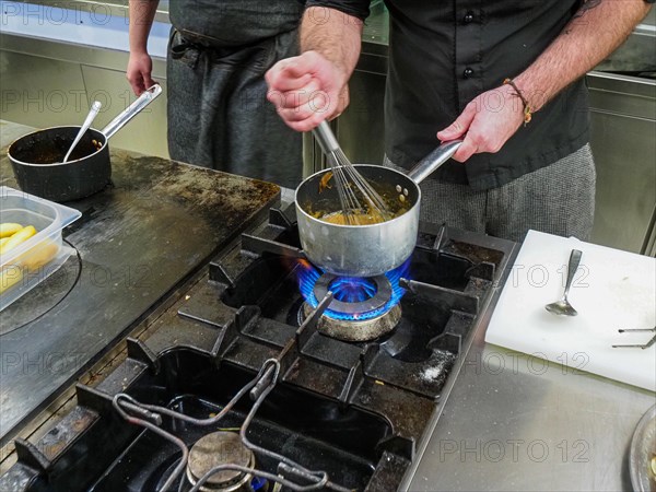 Chef using a hand mixer making a potato sauce cream reduction in a professional kitchen of a restaurant