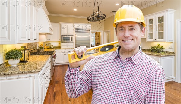 Smiling contractor with level wearing hard hat standing in custom kitchen