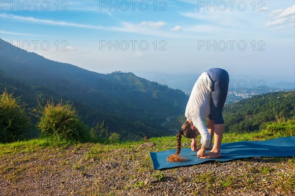 Young sporty fit man doing yoga Sun salutation Surya Namaskar pose Uttanasana outdoors in mountains