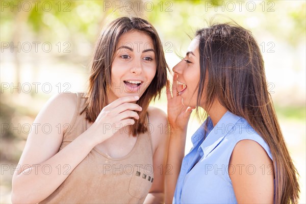 Two beautiful ethnic twin sisters whispering secrets outdoors
