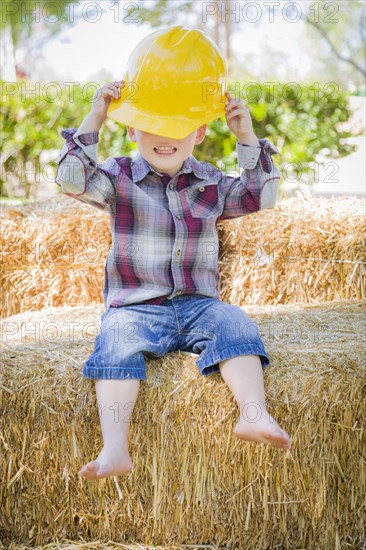 Cute young mixed-race boy laughing with hard hat outside sitting on hay bale