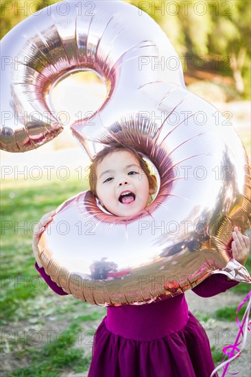 Cute baby girl playing with number three mylar balloon outdoors