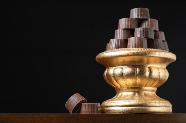 Stack of fine chocolates on golden pillar dish with dark background