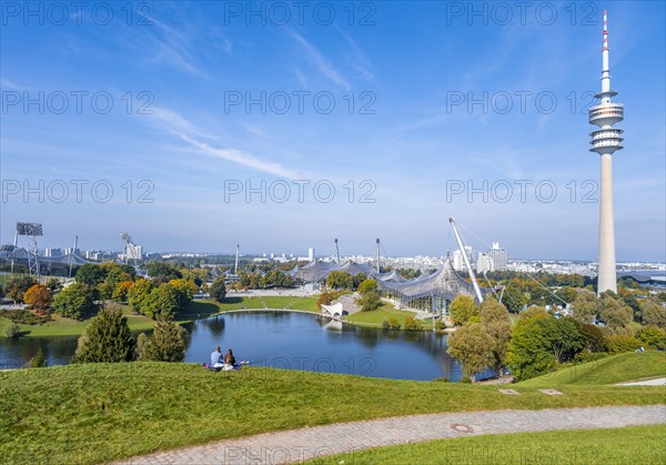 Two people sitting in the park with Olympic lake and Olympic tower