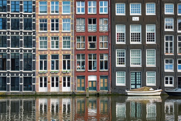 Row of typical houses and boat on Amsterdam canal Damrak with reflection. Amsterdam