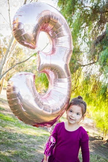 Cute baby girl playing with number three mylar balloon outdoors