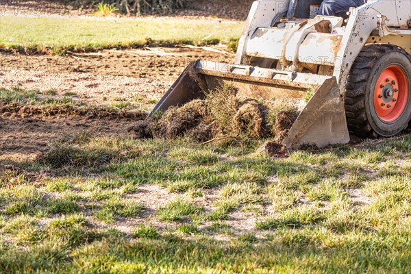 Small bulldozer removing grass from yard preparing for pool installation