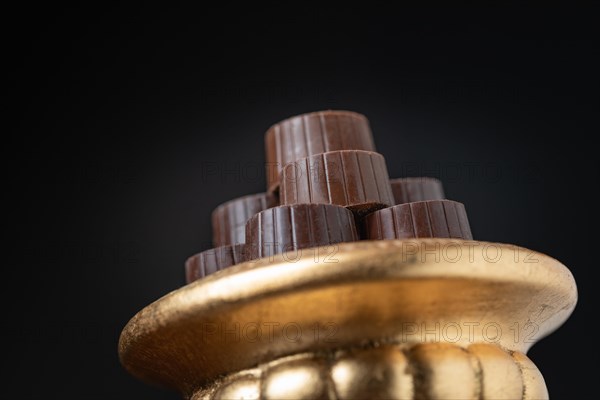 Stack of fine chocolates on golden pillar dish with dark background