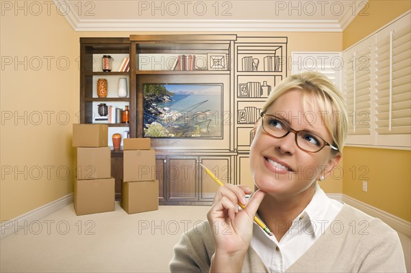 Female holding pencil in room with moving boxes and drawing of entertainment unit on wall