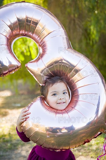 Cute baby girl playing with number three mylar balloon outdoors