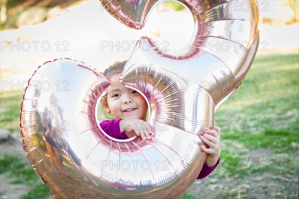 Cute baby girl playing with number three mylar balloon outdoors
