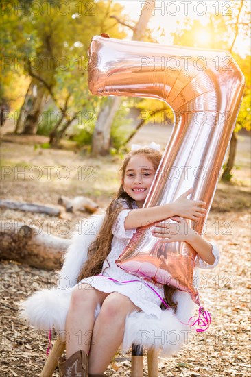 Cute young girl playing with number seven mylar balloon outdoors