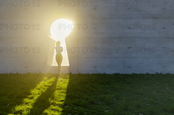 Woman standing at bright sun light shining through keyhole in concrete wall in grass and rocks field