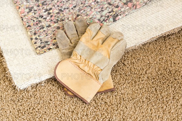 Construction gloves on pulled back carpet and underlay in room