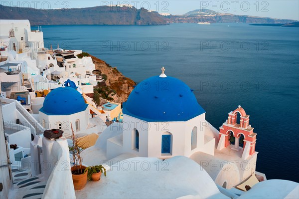 Famous view from viewpoint of Santorini Oia village with blue dome of whitewashed greek orthodox Christian church of traditional greek architecture